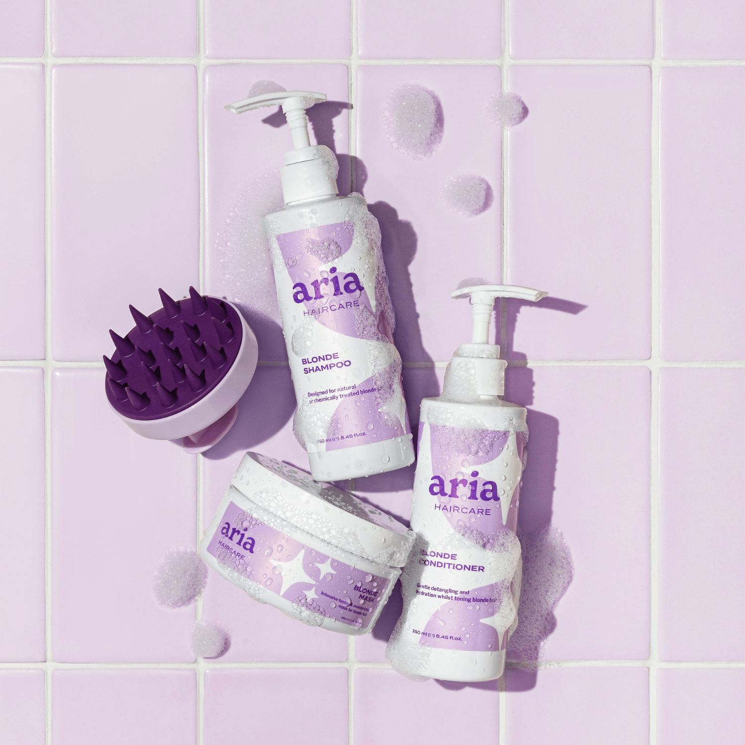 Aria haircare bright and blonde trio products including blonde shampoo, conditioner, and a scrub on a purple tiled background