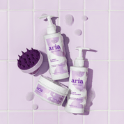 Aria haircare bright and blonde trio products including blonde shampoo, conditioner, and a scrub on a purple tiled background