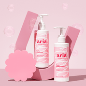 Aria haircare curl shampoo and conditioner bottles on a pink background with bubbles.