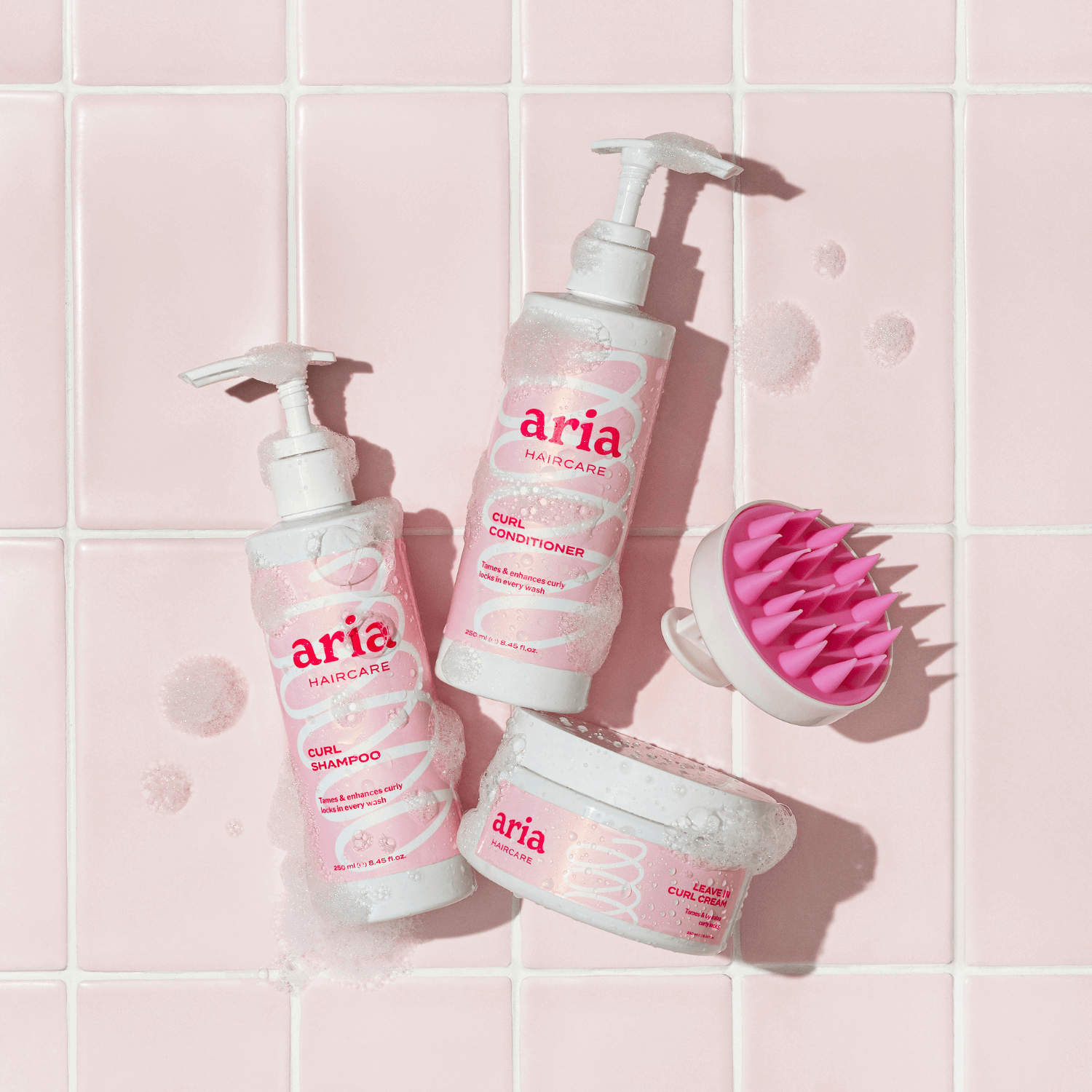 Aria haircare products including curl shampoo, curl conditioner, and curl cream on a pink tiled bathroom background