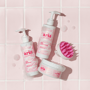 Aria haircare products including curl shampoo, curl conditioner, and curl cream on a pink tiled bathroom background