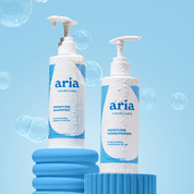 Aria Haircare hydrate shampoo and conditioner bottles on a blue background with bubbles.