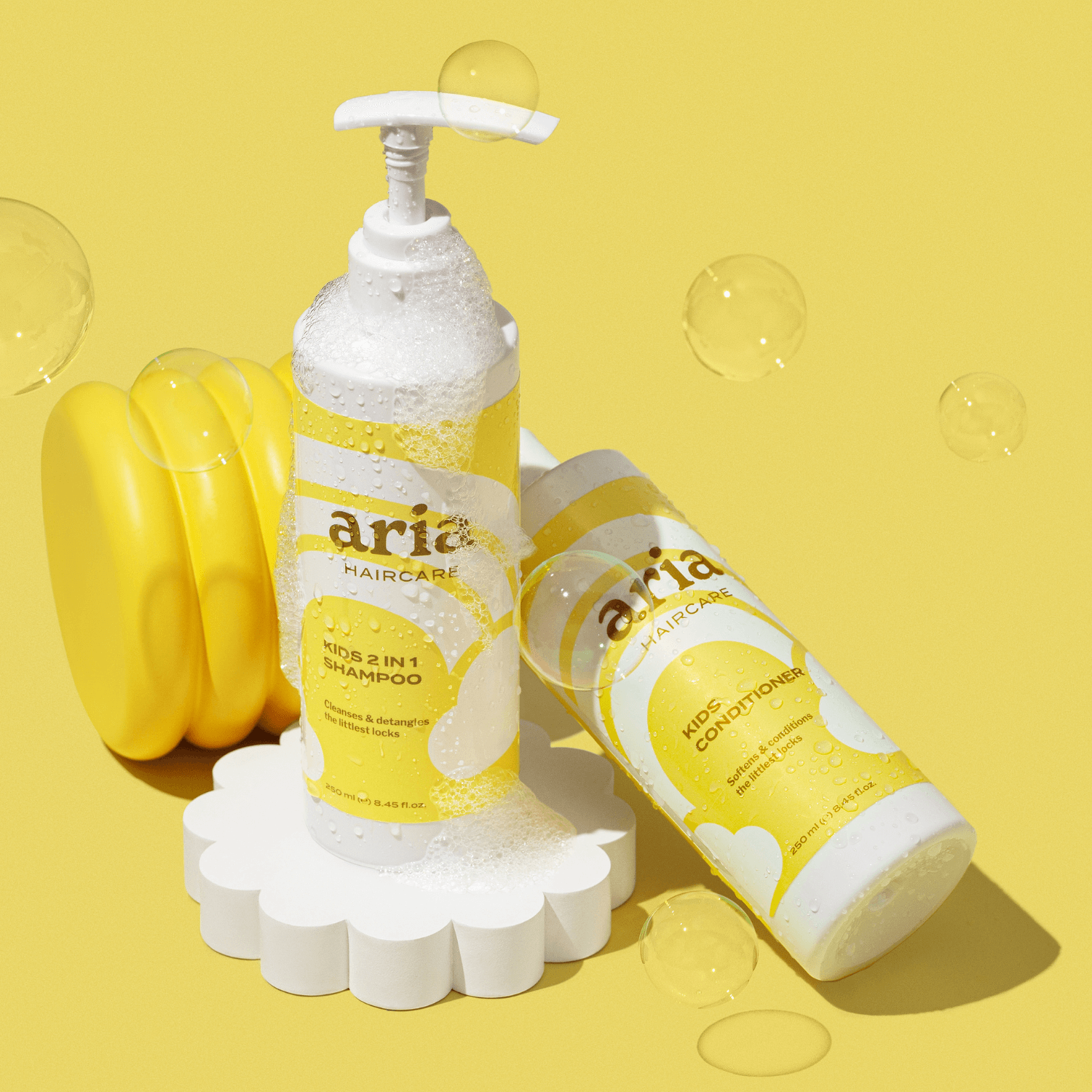 Aria haircare products including little locks duo kids 2 in 1 shampoo and conditioner on a yellow background with bubbles.