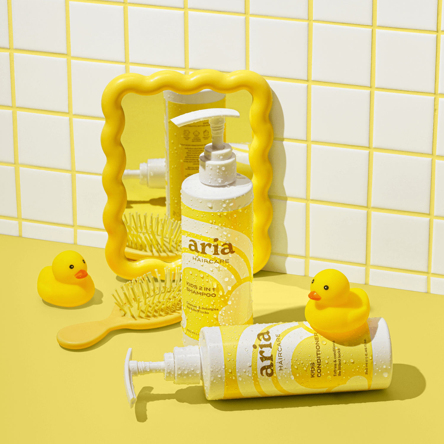 Aria haircare little locks duo kids products with a yellow rubber duck and mirror on a yellow tiled background