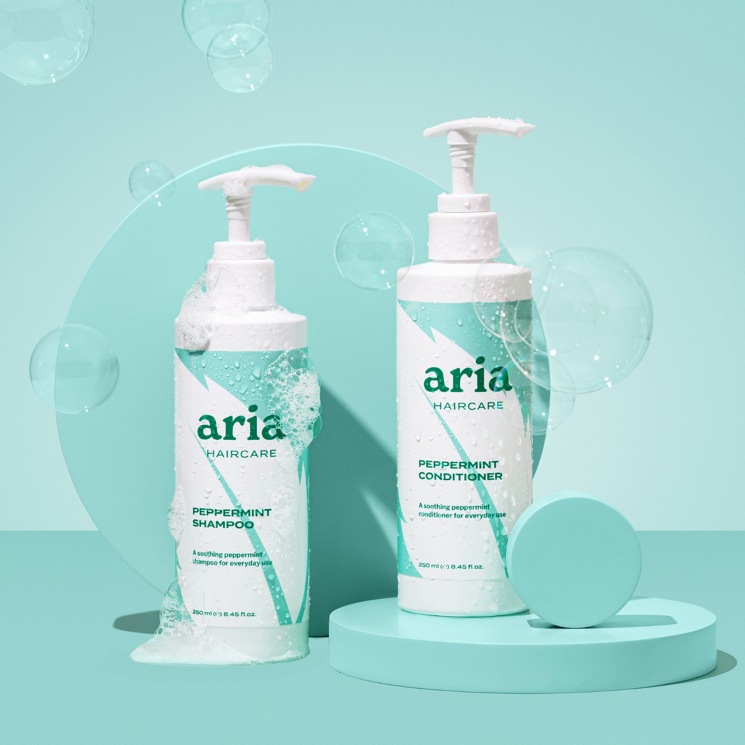 Aria haircare scalp therapy duo peppermint shampoo and conditioner bottles on a light blue background with bubbles